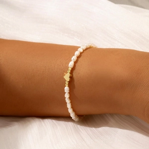 Dettaglio del bracciale di perle barocche con ciondolo a cuore dorato indossato al polso