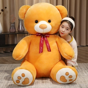 Detail of a giant orange teddy bear plush toy with a red ribbon in a cozy room