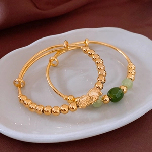 Detailed macro of 18k gold plated PiXiu bangles with jade beads in a ceramic dish