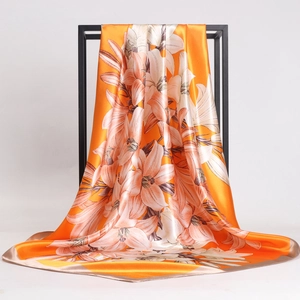 Orange silk square scarf with white lily print hanging on a black display frame