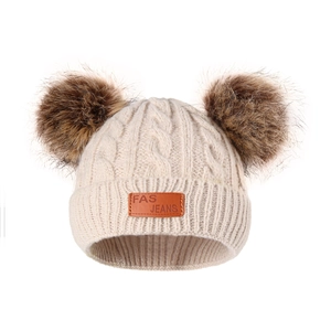 Detailed close-up of beige knitted baby hat featuring dual brown pom-poms and leather patch