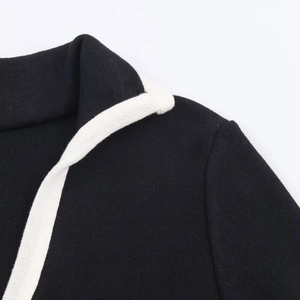 Detailansicht des schwarzen Strickkleid-Ausschnitts mit weißer Kontrastpaspelierung