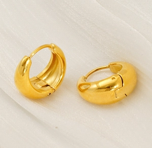 Detailed view of thick gold-plated huggie hoop earrings with polished mirror finish
