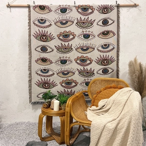 Detail of bohemian eye pattern tapestry with tassels hanging on a textured white wall