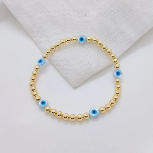 18K gold plated beaded bracelet featuring natural shell evil eye charms on white fabric