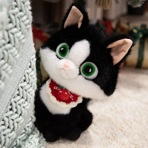 Cute black and white tuxedo cat plush toy with red strawberry bib sitting on cozy blanket