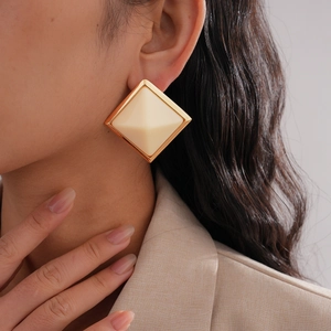 Detailed close-up of large geometric diamond-shaped earring in gold and beige resin finish