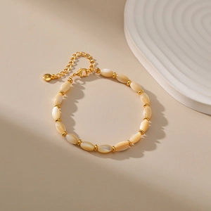 Detail of cream shell beads and 18K gold-plated chain bracelet on aesthetic background