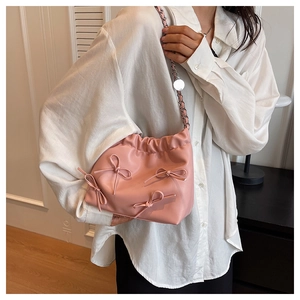 Detail of pink leather bucket bag featuring a decorative bow and elegant metal chain