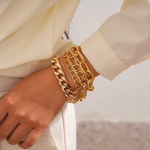 Detail of layered gold chunky chain bracelets styled with a silk blouse for a chic look