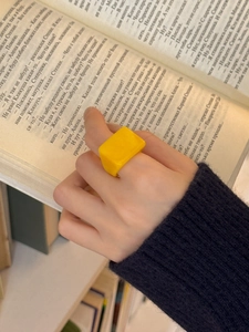 Gros plan d'une bague carrée minimaliste en résine jaune sur un doigt avec un livre.