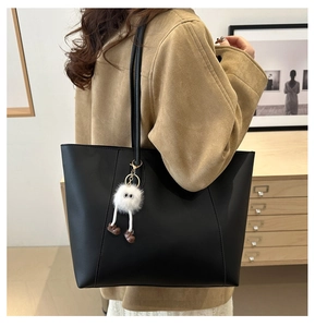 Detail of a black leather tote bag featuring a cute white plush monster charm on the shoulder strap