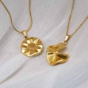 Gold stainless steel necklaces featuring floral and abstract pleated pendants on white fabric