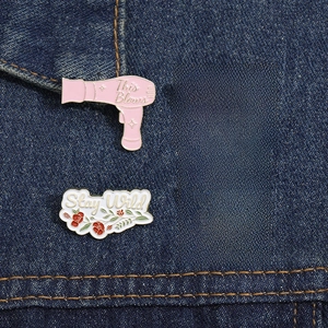 Close-up of four fun cartoon enamel pins with text on dark blue denim fabric texture