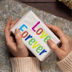 Detail of 1.5 inch alphabet stickers on a wrapped gift box held by hands in warm setting