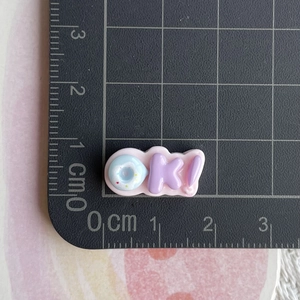 Mini resin charm featuring OK letters with donut shape on a centimeter scale pad