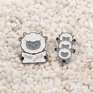 Close-up of cute lamb enamel brooches with Make a Wish sign on white pebbles