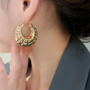 Close-up of a woman wearing gold-plated hoop earrings with a textured hammered finish