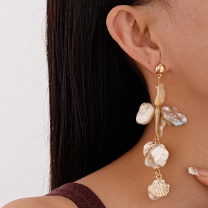 Close-up of dangling ocean-style earrings with mother-of-pearl and golden shell charm