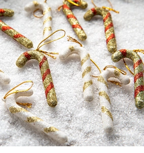 Detail of red and white glitter candy cane ornaments on a snowy Christmas tree background