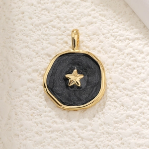 Detail of a round gold pendant with black enamel inlay and a tiny gold star charm