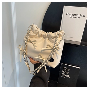 Detail of a beige PU leather drawstring bucket bag with decorative bows and chain strap