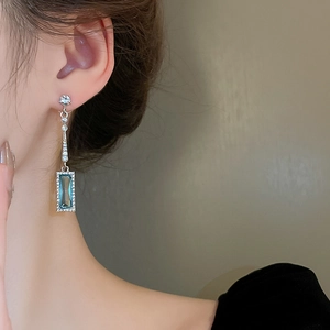 Close-up of geometric silver needle earrings with blue square crystals and diamonds