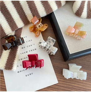 Detail of assorted acetate bow hair claws on a wooden surface with lifestyle props