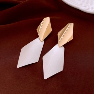 Detail of geometric two-tone metal earrings in gold and silver finish on red velvet