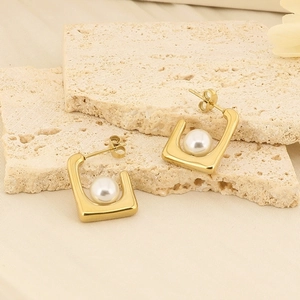 Detail of square gold pearl earrings on beige stone and fabric background with soft light