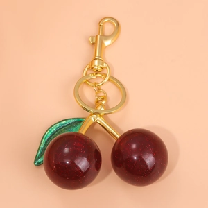 Glittery dark red cherry keychain with green leaf and golden lobster clasp on beige base