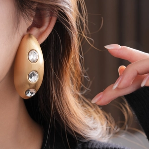 Macro shot of gold oval earrings with crystals on model's ear showing matte texture