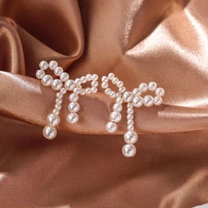 Detailed close-up of bow-shaped pearl earrings with elegant tassels on champagne silk