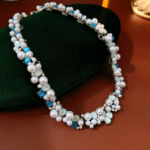Dettaglio collana vintage con perle bianche e gemme blu su velluto verde scuro