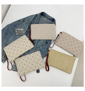 Flat lay of five straw and canvas clutch bags with daisy prints and wrist straps