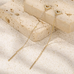 Macro detail of gold-plated long chain heart earrings on a natural beige stone