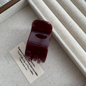 Detail view of a burgundy glossy hair claw clip on a minimalist textured surface