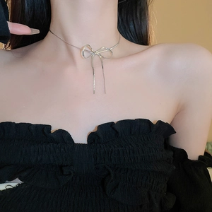 Detail of silver bow pendant necklace with long fringes on elegant female collarbone