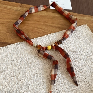 Close-up of retro orange plaid fabric headband with elegant bead accents and ribbons