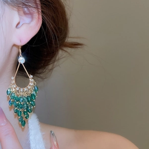 Detail of luxury gold drop earrings with clear zircon and green beaded crystal tassels