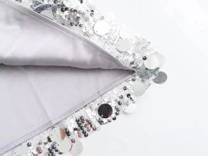 Close-up of silver sequins on white lace with satin lining on a mini dress