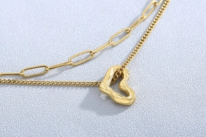 Detail of gold double-layer necklace with paperclip chain and hollow heart pendant