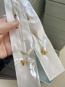 Detail of two gold puppy and corgi pendants necklaces in transparent OPP packaging