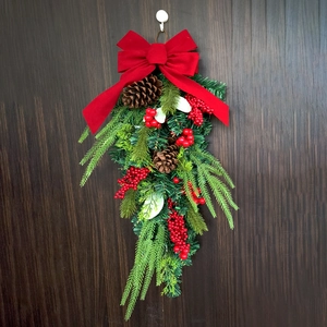 Christmas teardrop swag with red velvet bow, pine cones and berries on wood background