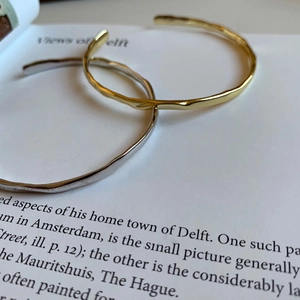 Irregular hammered 925 sterling silver open bangle in gold and silver finish on a book