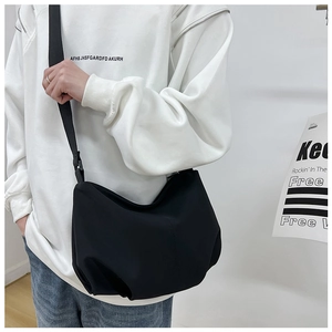 Detail of minimalist black pleated crossbody bag with wide adjustable strap on model