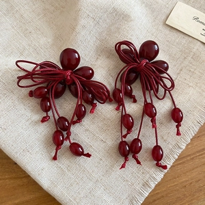 Detail of dark red resin bow earrings with tassel on natural linen background