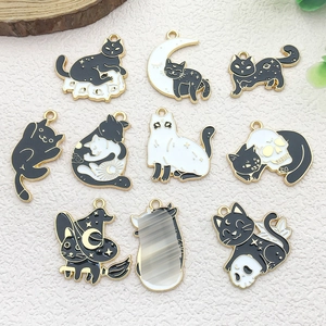 Detailed flat lay of black and white enamel Halloween cat charms with gold edges and moon motifs