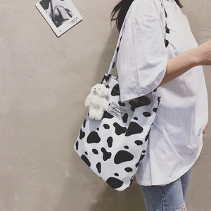 Detail of cow print canvas tote bag with Augur brand label and plush bear keychain