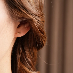 Detailed close-up of a delicate gold plated bar earring with pavé zircon on woman's ear